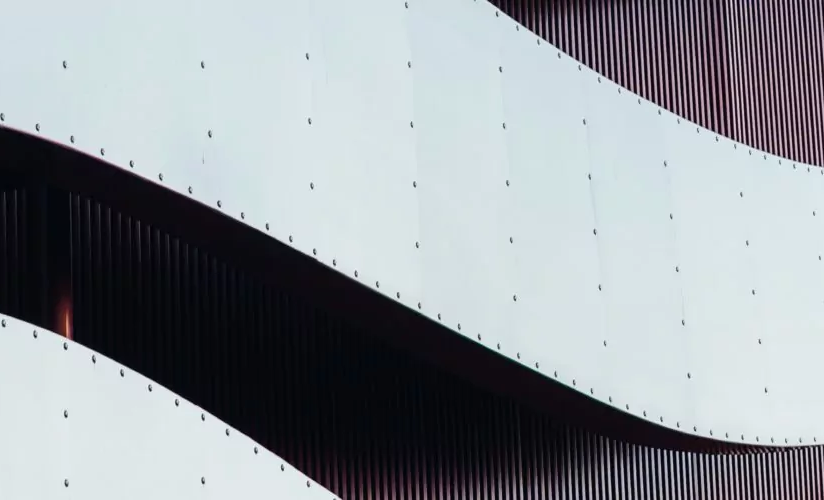 Metallische Wellenform vor einer Hausfassade.